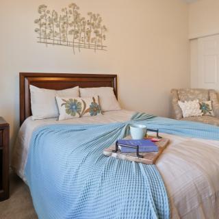 A cozy bedroom with a neatly made bed adorned with blue and white bedding, decorative pillows, and a wooden tray holding books and a mug.