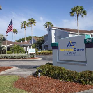 Exterior view of a building with a prominent sign, surrounded by palm trees and an American flag.