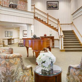 A spacious lobby featuring a grand piano, elegant staircase, and comfortable seating with floral decor.