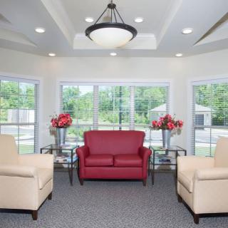A modern living room featuring a central red sofa, beige armchairs, and large windows that allow natural light to fill the space.