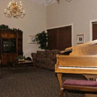A cozy living room featuring a piano, chandeliers, and comfortable seating.