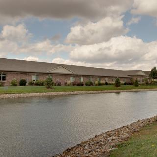 A wide landscape view of a building by a pond under a cloudy sky.