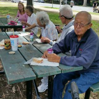 A group of elderly individuals enjoying a picnic at a park table.
