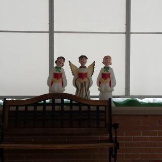 Three choir angel figurines displayed on a bench indoors.