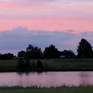 A serene sunset reflecting on the water, surrounded by trees and an expansive sky.