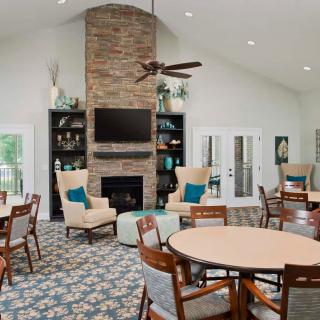 A cozy community room with a fireplace, seating area, and tables for gatherings.