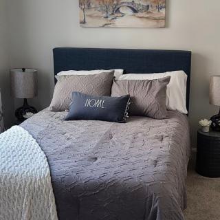 A neatly made bed in a well-decorated bedroom with lamps on each side and a painting above the headboard.