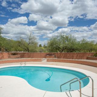 A serene outdoor swimming pool surrounded by desert landscape under a partly cloudy sky.