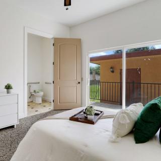 A minimalist bedroom with a neatly made bed, green accent pillows, and sliding glass doors leading to an outdoor view.