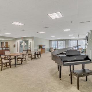 A spacious and well-lit lounge area featuring a grand piano, tables, and chairs.