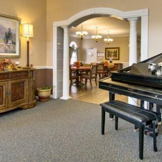 A cozy living room featuring a grand piano with a bench, elegantly decorated with artwork, furniture, and an archway leading to another room.