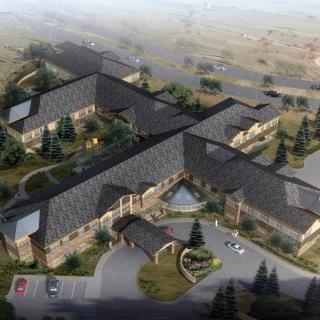 Aerial view of a large building complex surrounded by trees and roads in a scenic landscape.