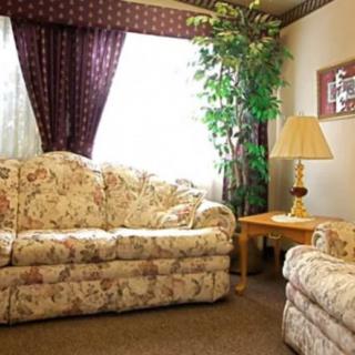 A cozy living room featuring floral sofas, a lamp on a wooden side table, with decorative curtains and an indoor plant.