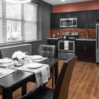 A stylish modern kitchen and dining area featuring sleek black cabinetry, stainless steel appliances, and a meticulously set dining table.