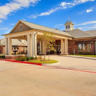 A modern building with a prominent entrance and a well-maintained driveway under a blue sky.
