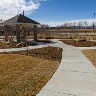 A well-maintained park with a concrete pathway leading to a pavilion under a clear blue sky.