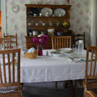 A cozy dining room with a table set for a meal, featuring a vase of flowers and a china cabinet in the background.