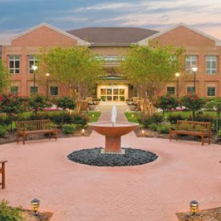 A serene courtyard featuring a fountain surrounded by greenery and benches, with a warm evening glow.