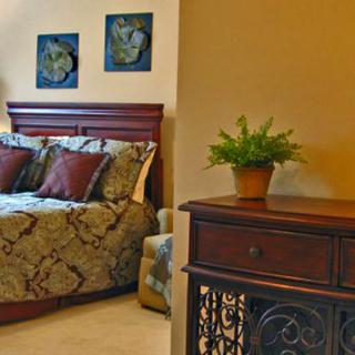 A cozy bedroom with a wooden bed and matching nightstand, adorned with decorative pillows and a potted plant.