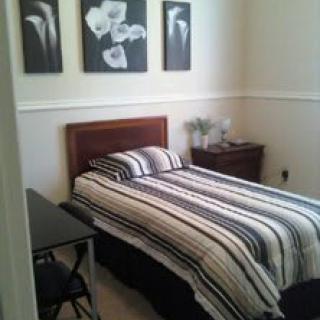 A cozy bedroom with a single bed featuring striped bedding, accompanied by a nightstand and floral artwork on the wall.
