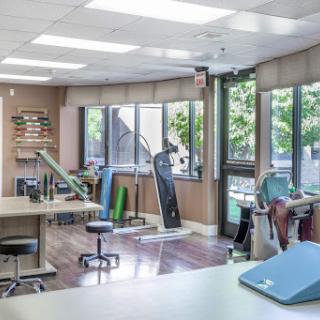 A spacious therapy room equipped with exercise machines and natural light from large windows.