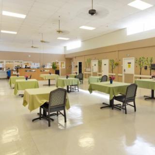 An empty cafeteria with green tablecloths and neatly arranged chairs.