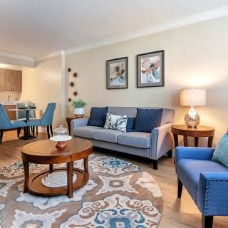 A cozy living room with a gray sofa, blue armchairs, and a round wooden coffee table, complemented by a dining area in the background.
