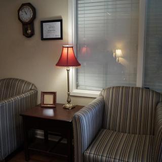 A cozy living room corner featuring two striped chairs, a side table with a red lampshade lamp, and a wall clock.
