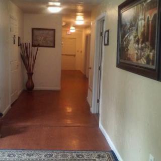 A well-lit hallway with wooden flooring, adorned with artwork and a decorative vase.