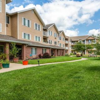 A residential apartment building with a well-maintained lawn and walkway under a partly cloudy sky.
