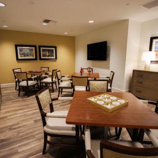 A cozy dining area with several tables and chairs, featuring warm lighting and a wall-mounted television.
