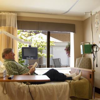 A patient relaxes in a hospital room while a visitor engages with them.