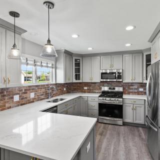 A modern kitchen featuring white countertops, gray cabinets, and stainless steel appliances.