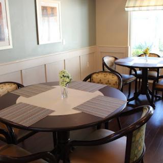A cozy dining area featuring round tables and comfortable seating, illuminated by natural light.