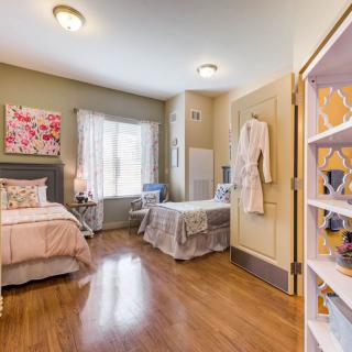 A cozy bedroom with two beds and bright natural light, featuring hardwood floors and decorative art.