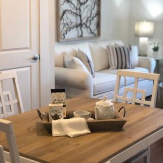 A cozy living room with a wooden dining table adorned with a decorative tray set, complemented by neutral-colored furniture and soft lighting.