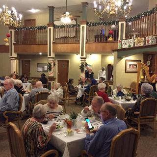 A group of elderly people enjoying a meal in a spacious, warmly decorated dining area.
