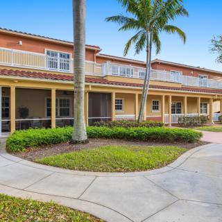 A two-story building with a landscaped walkway and palm trees in front.