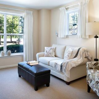 A cozy living room with a sofa, patterned chairs, and an ottoman by a large window letting in natural light.