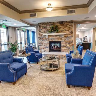 A modern living room with blue armchairs arranged around a glass coffee table, centered by a stone fireplace.