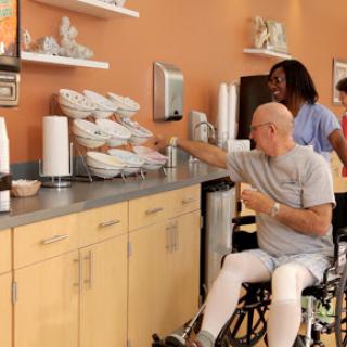 A caregiver assists an elderly individual in a wheelchair at a snack station.