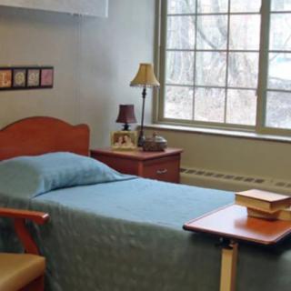 A simple bedroom with a single bed, bedside table, and a window.