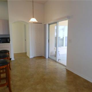 A minimalist kitchen and dining area with tile flooring, pendant lighting, and sliding glass doors.