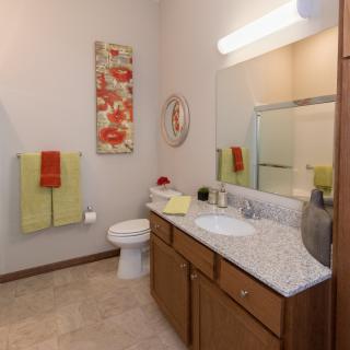 A well-organized bathroom with a sink, mirror, and shower, featuring colorful towels and wall decor.