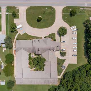 An aerial view of a building with an adjacent parking lot, surrounded by trees and grass.
