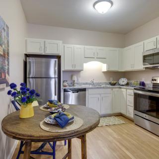 A modern kitchen with a small dining area featuring stainless steel appliances and white cabinetry.