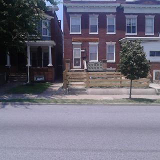 A street view of a brick residential house with a small front yard and a tree.