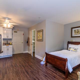A cozy bedroom with wooden flooring, featuring a single bed and a kitchenette.