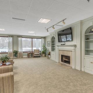 A cozy living room with a fireplace and television, featuring comfortable seating and large windows.