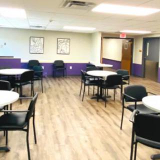 An empty cafeteria with tables and chairs, featuring wood flooring and bright lighting.